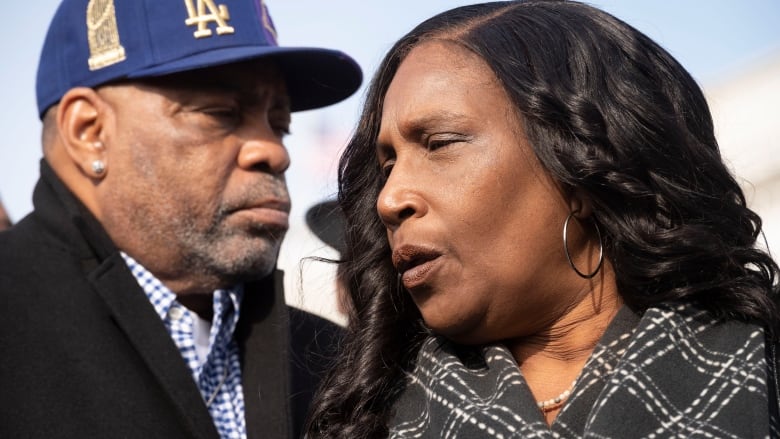 A man wearing a blue ball cap stands with a woman in a black and white scarf.