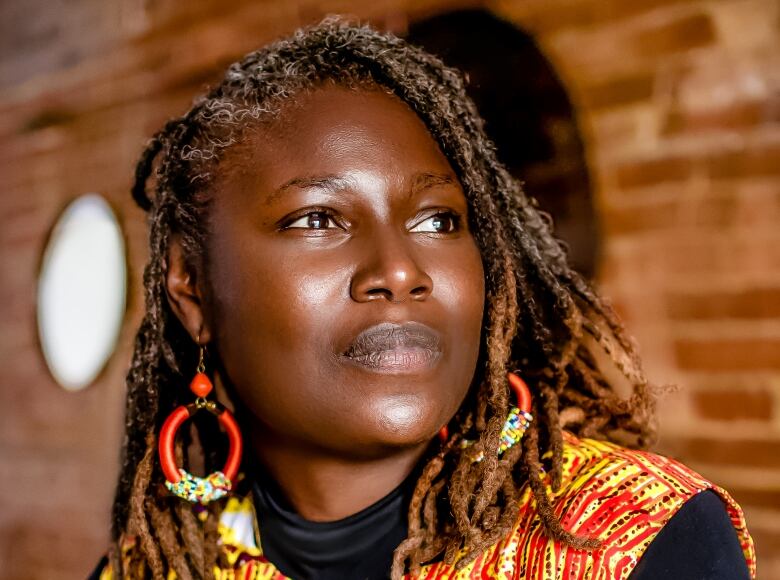 A Black woman in orange looks past the camera.