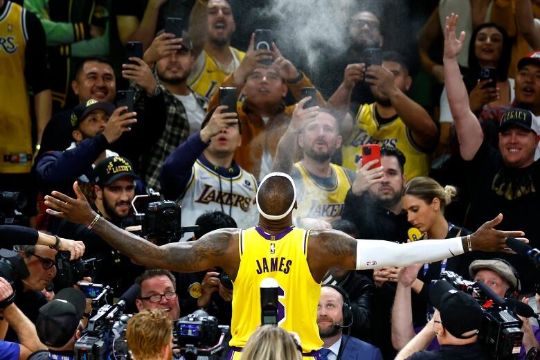 A basketball player has his hands wide open as is seen doing his famous pre-game routine in which he throws chalk in the air in front of the fans.