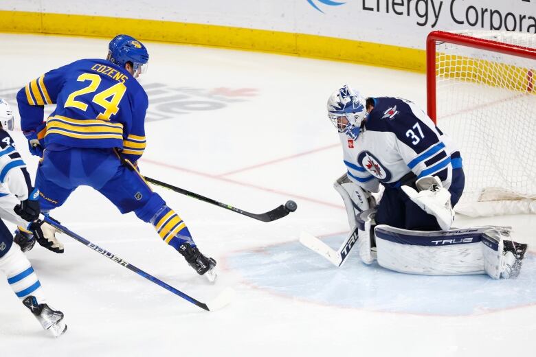 Hockey player with puck on the tip of his stick, goalie looking down.