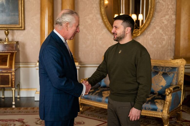 Two adults shake hands in front of a couch.