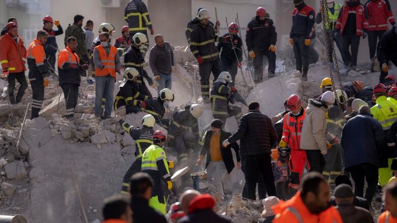 Dozens of rescue workers stand on a pile of rubble.