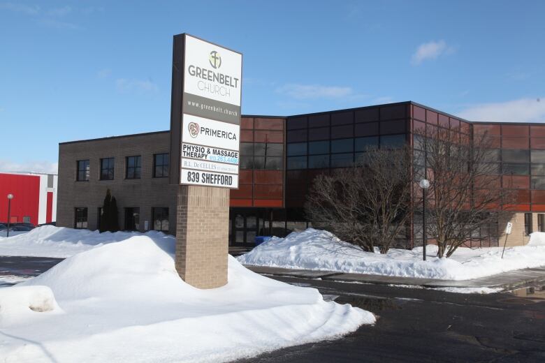 A sign with various business names stands in a snowbank in front of a suburban office building.