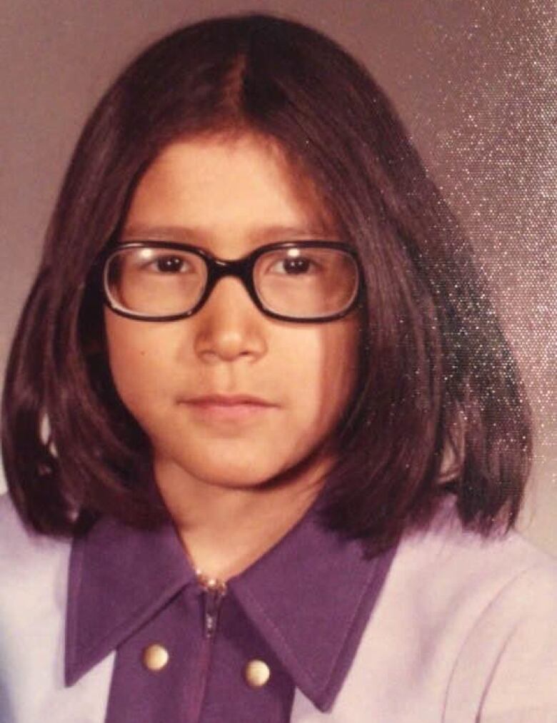 A young girl with glasses poses for a photo.