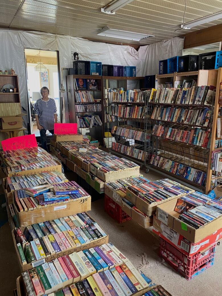 A woman stands in a doorway to a room filled with used books