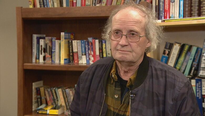 A man stands in front of a book shelf.