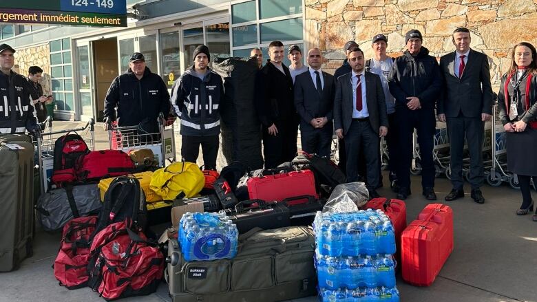 A group of men stand with large suitcases at an airport.