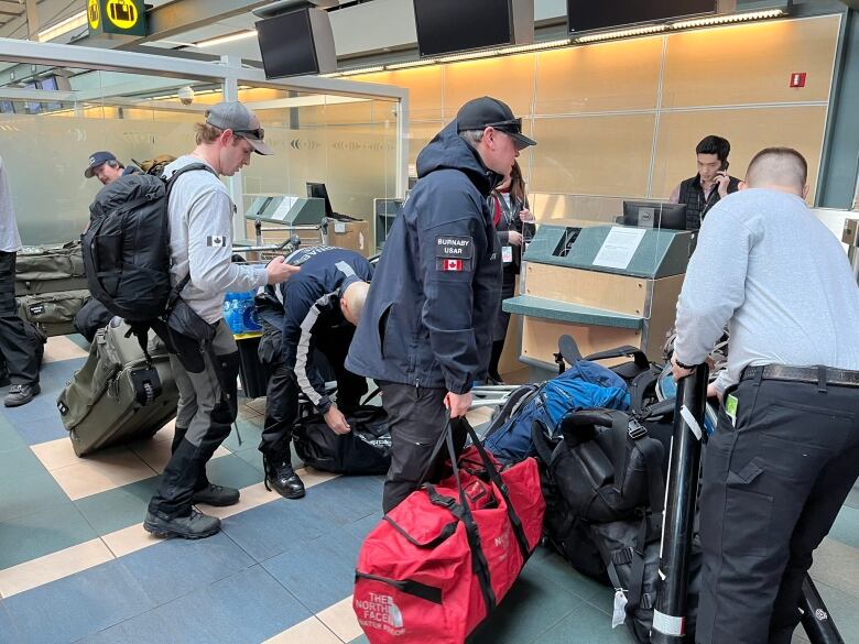 Men with large duffel bags stand at a check-in counter at an airport.