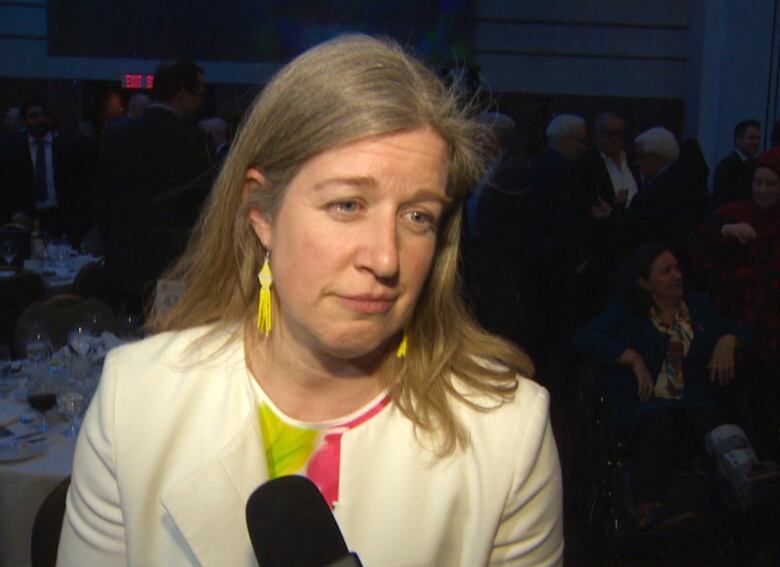 A woman listens to a reporter's question during an interview in a hotel ballroom. 