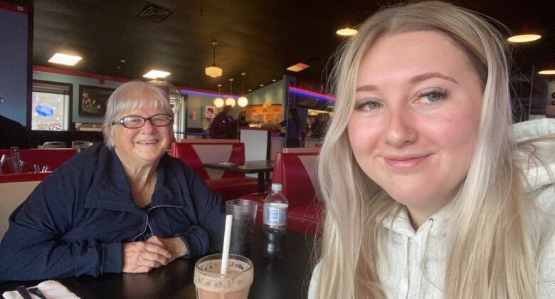 An elderly woman and a young woman smile in a selfie in a restaurant. 