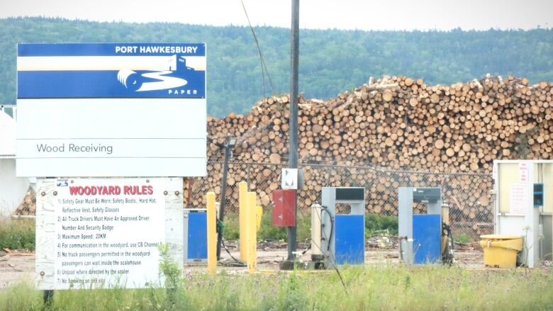 A sign listing wood yard rules stands in front of a stack of cut trees.