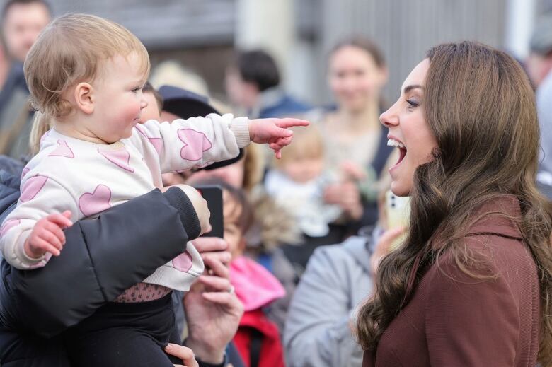 An adult laughs as a child held by another adult points.