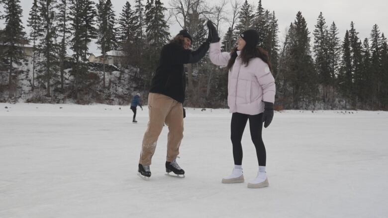 A man and a woman stand on an ice rink high-fiving.