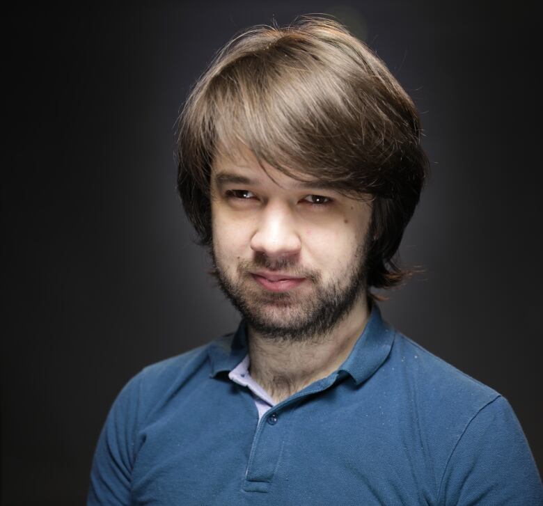 A man with shaggy brown hair wearing a blue polo shirt.