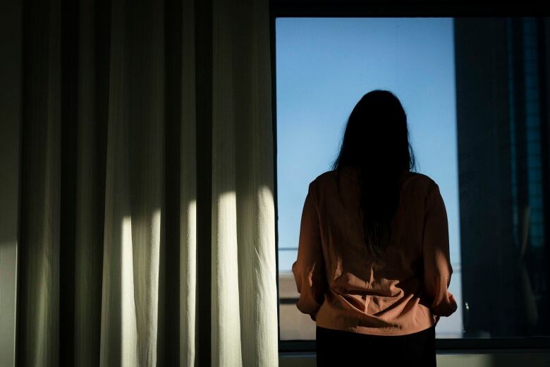  Woman stands in shadow in front of a window.