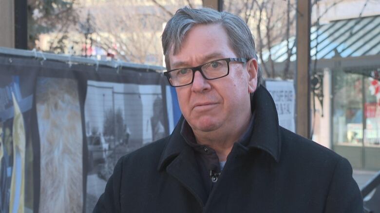 a man with grey hair in a black coat stands outside