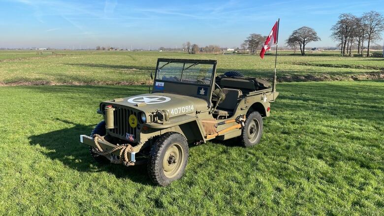 A picture of a military jeep, a Canadian flag hanging off it's radio antenna, sitting in a field in the Dutch countryside.