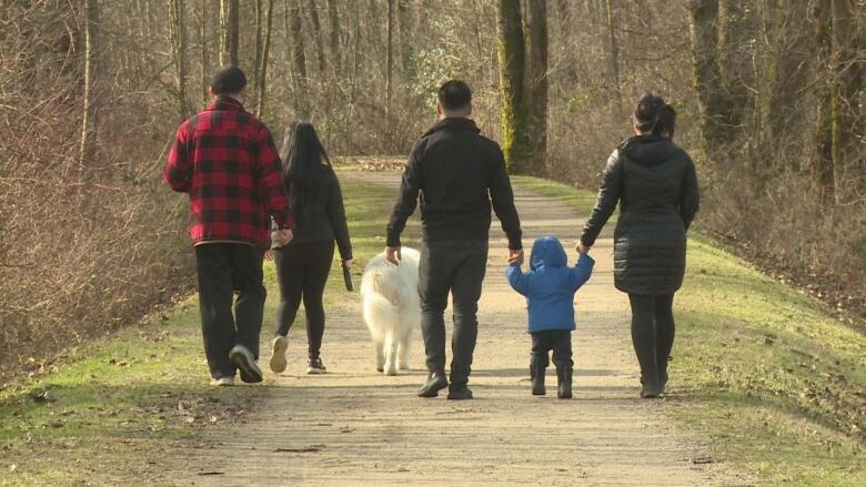 A shot of a family, including a child and a dog, walking in a park.