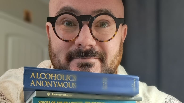 A man holds onto a large stack of books focused on treatment for drug and alcohol addiction.