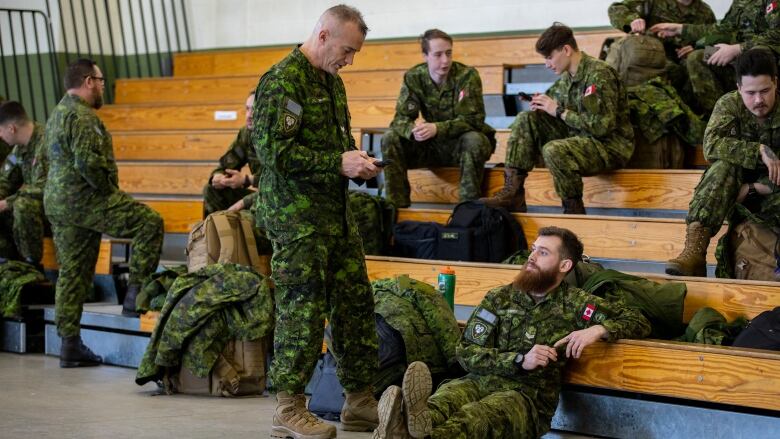 Soldiers sit around with their gear in a gym.