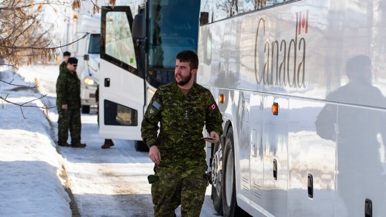 A soldier walks by a bus taking soldiers on deployment.