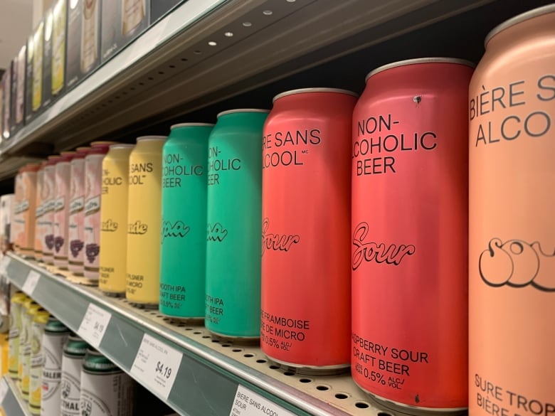 A series of multi-coloured rainbow cans full of alcohol free beer on a shelf.