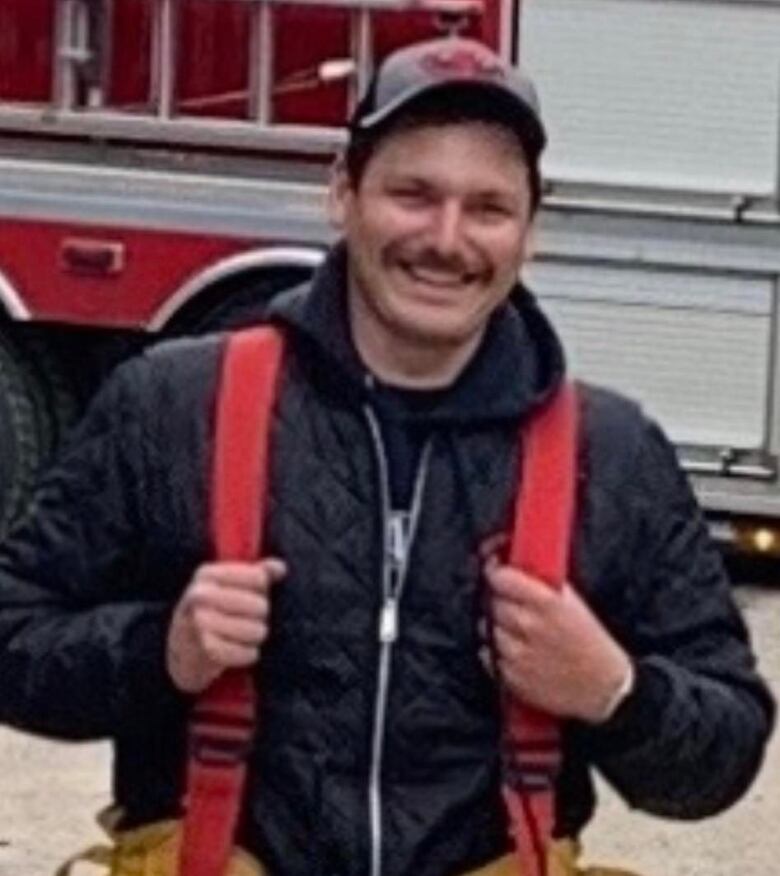 A man with red suspenders stands in front of a firetruck, smiling for a photo