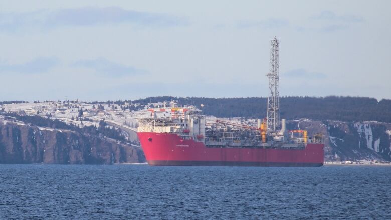 A small blue and white boat tows a large red vessel with industrial equipment on deck.