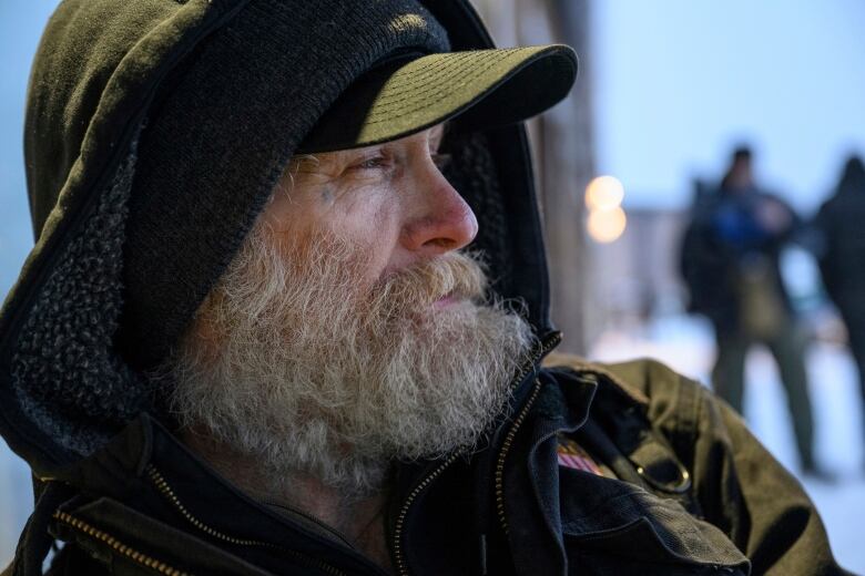 Profile of bearded man in hoodie, ball cap.