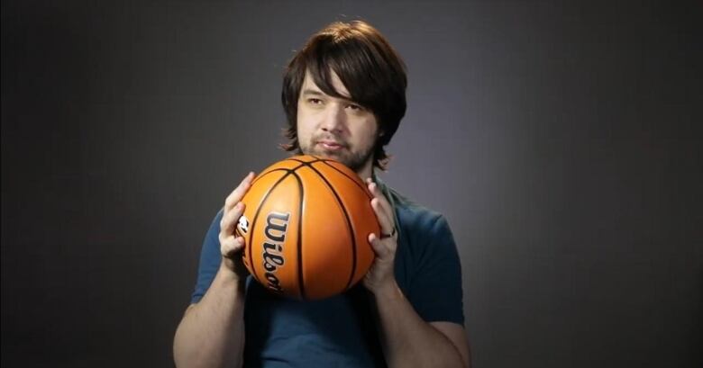 A young man holds a basketball up to his chest.