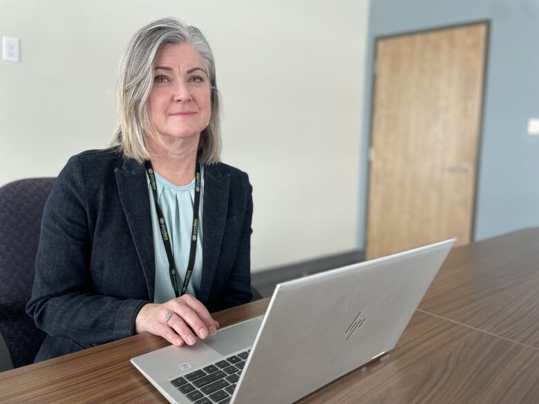 A woman in a blazer sits at a laptop on a desk.