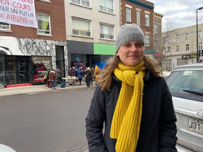 A woman stands across the street from a demonstration. 