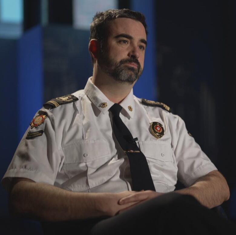 Fire Marshal Mike Lewis wearing a white uniform and black tie sitting with his hands folded. 