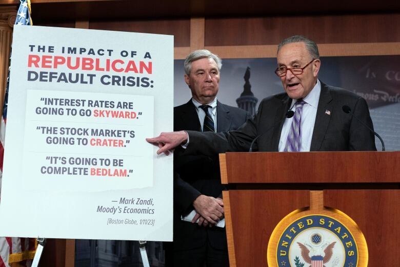 Grey haired man with galsses stands at podium with a sign beside him that says 'The impact of a Republican debt crisis' 