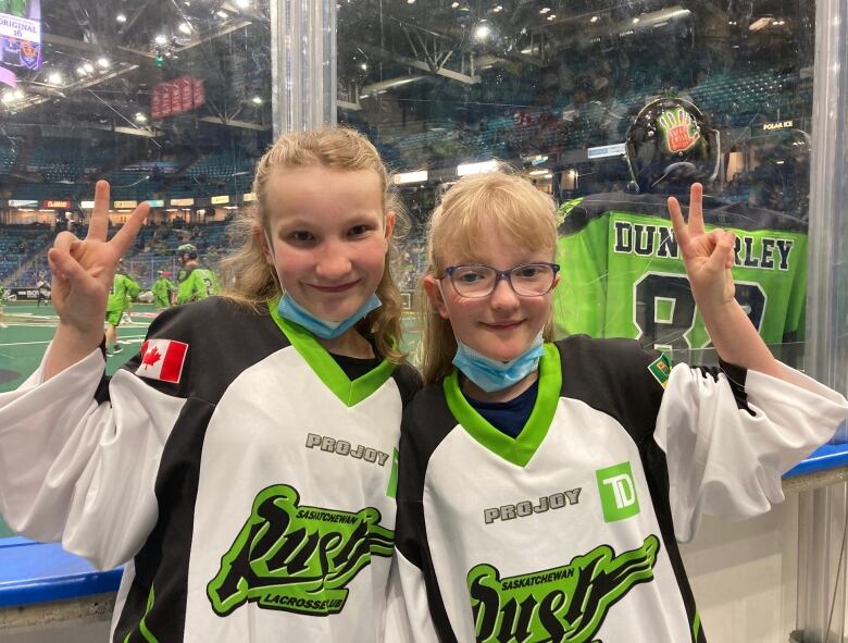 Two blond girls stand dressed in Saskatchewan Rush lacrosse jerseys. 