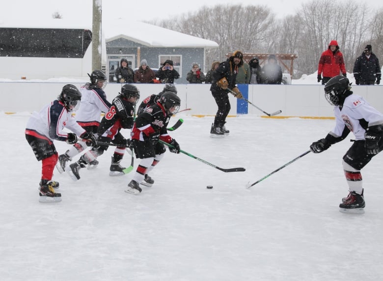 Teams in Black and white jersey race down an outdoor ice rink at a skills hockey camp hosted by Ted Nolan and his two sons.