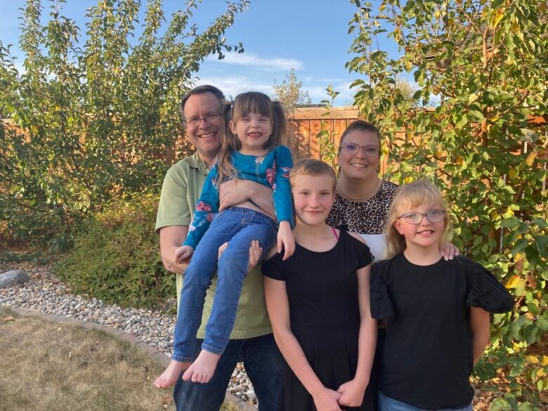 A man and woman stand in their backyard along with their three daughters.