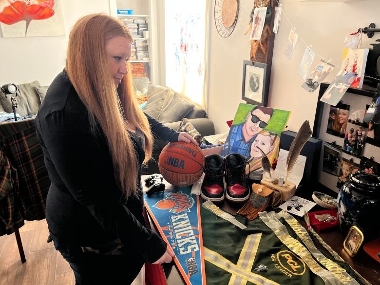 A woman stares at a table full of memorabilia laid out on her kitchen table, stuff her husband loved including basketballs and family pictures.