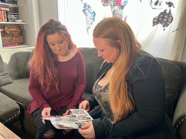 Two women sit on a soft looking at photos.