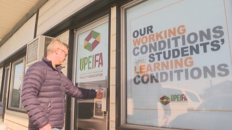 Man in puffy jacket opens door to an office with a sign in the window reading: 