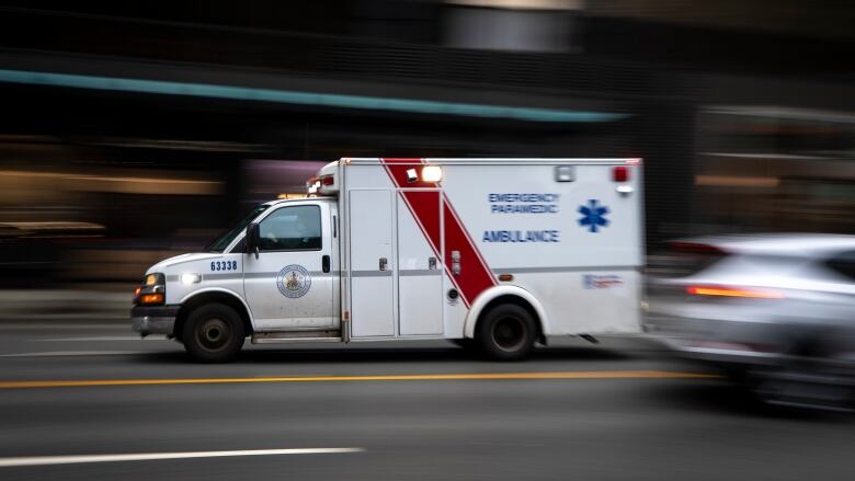 An ambulance going down the road and a car passing in the opposite direction both will blurred backgrounds suggestive of speed.