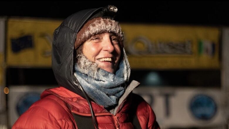 A smiling woman in a headlamp and a parka stands outside in the dark.