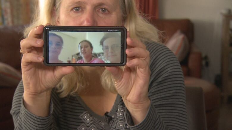 Olga Ostapiv holds up a phone showing Yuliia, Anastasiia and Maksym, who speak with CBC News from Puerto Vallarta, Mexico.