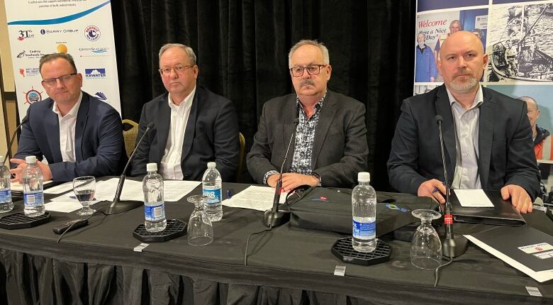 Four men sit at a table with microphones in front of them.