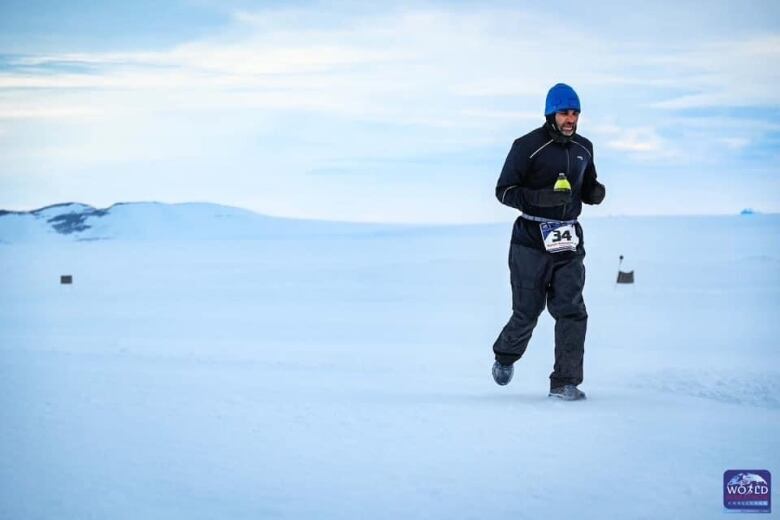 A man in a hat, jacket and snowpants runs across a snow-covered landscape.