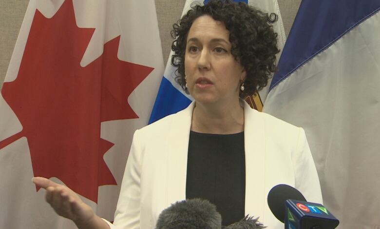 A woman with dark curly hair stands in front of Nova Scotia and Canada flags.