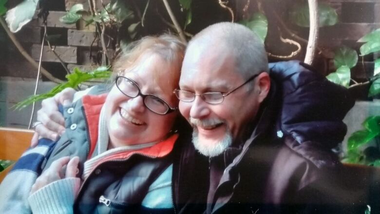 A man and woman smile sitting on a bench with leaves cascading behind them.