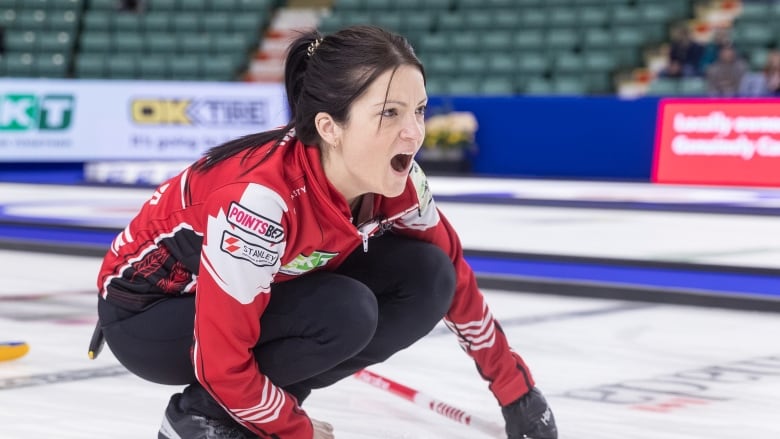 A women's curling skip crouches while directing during a match.