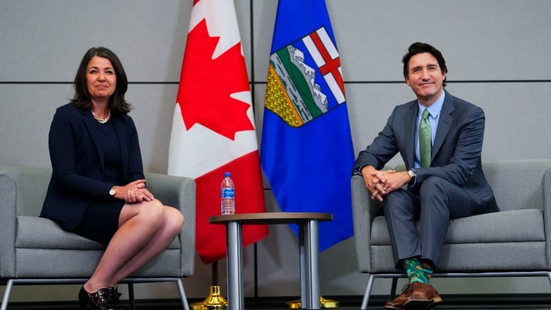 A woman with brown hair sits in a chair next to a man with black hair in a blue suit