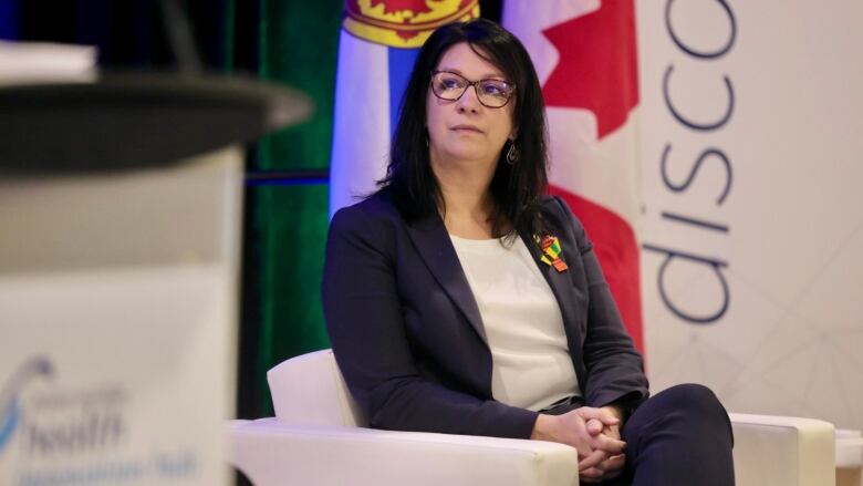 A woman sits in a white chair in front of a Canadian and Nova Scotian flag.